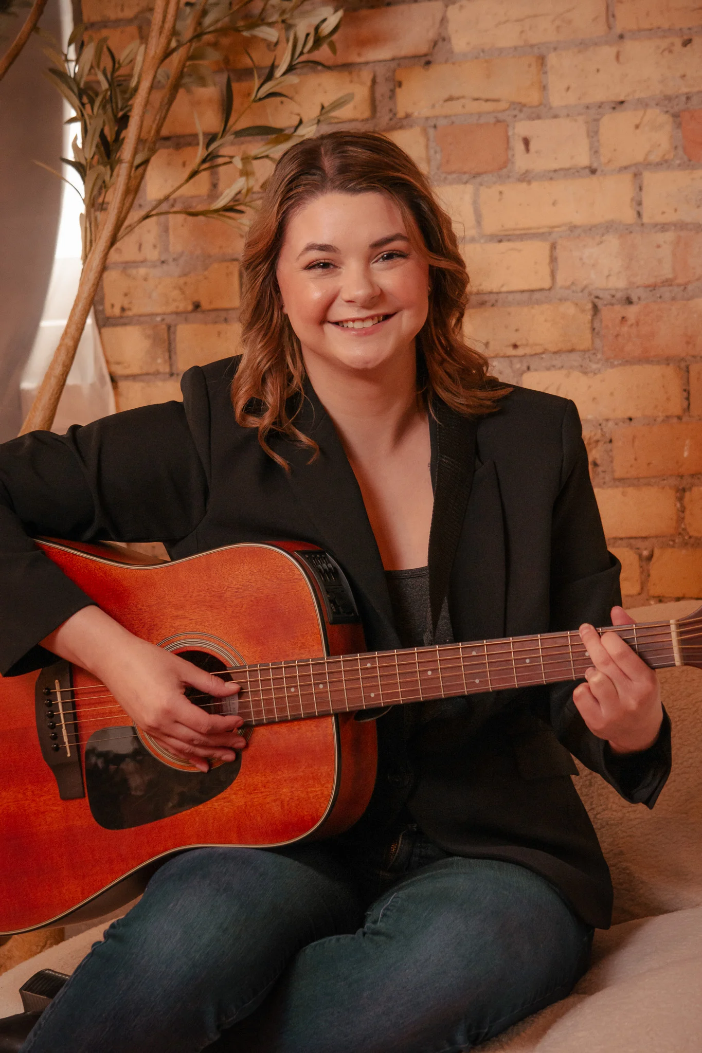 Portrait of a smiling woman playing an acoustic guitar in front of brick
